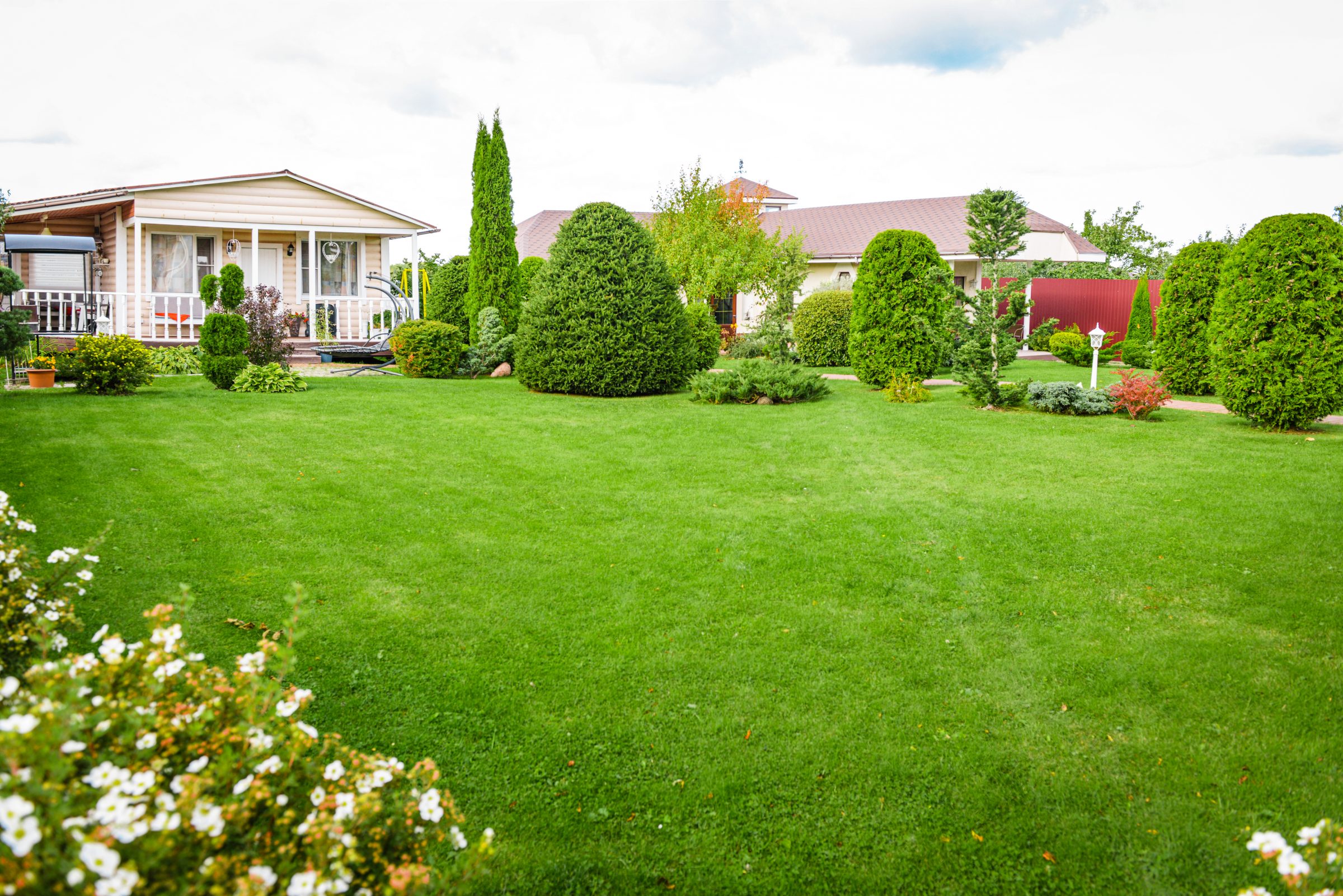 A well-maintained garden with lush green grass, bushes, and a small porch-style house set amid vibrant, neatly arranged plants and shrubs.